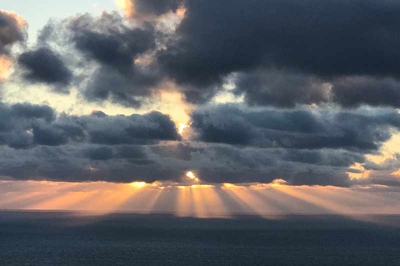 A photo of a sunset, the rays forming bars as they pass through a cloud.